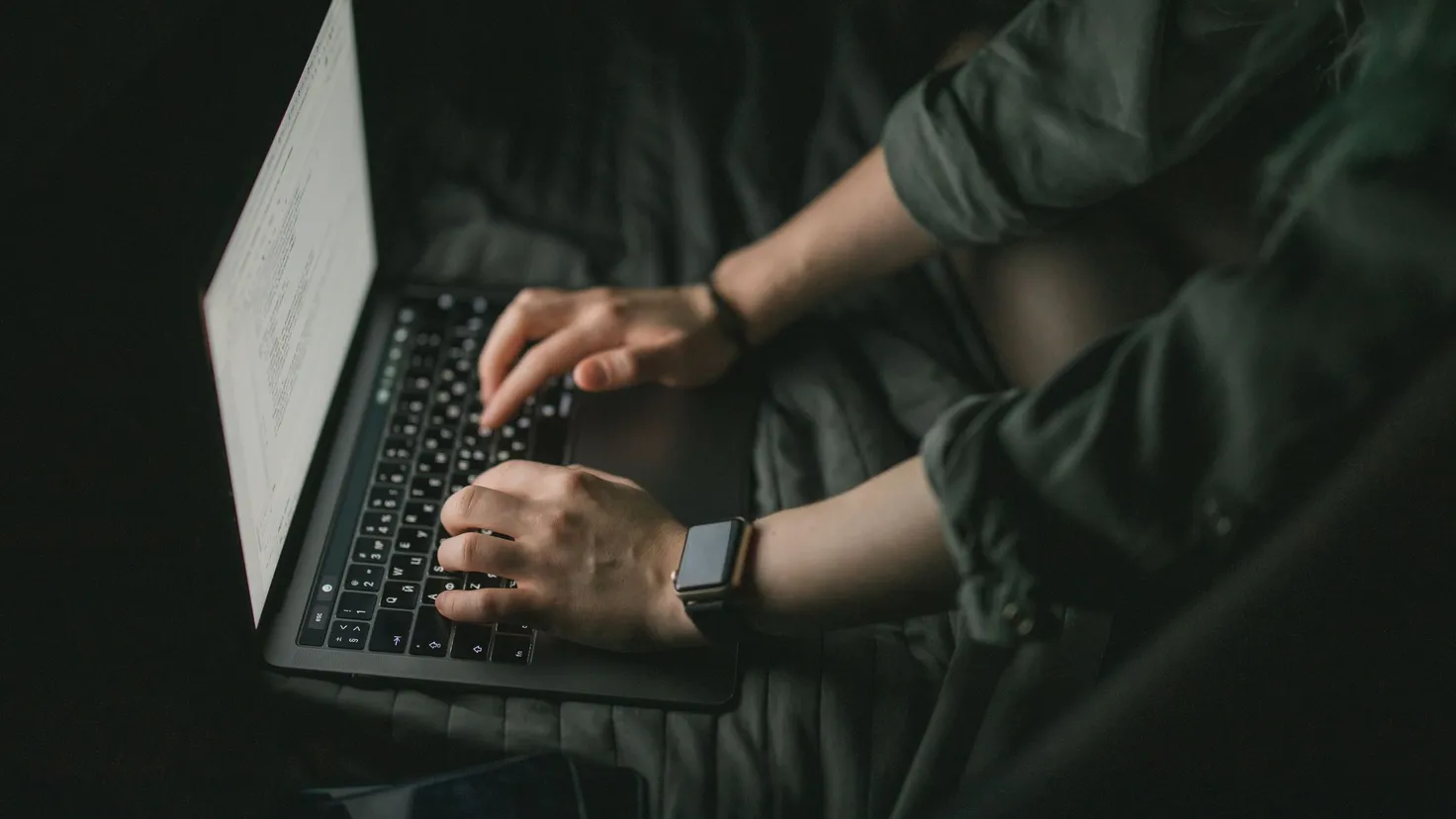 Dłonie piszące na klawiaturze laptopa w ciemnym pomieszczeniu